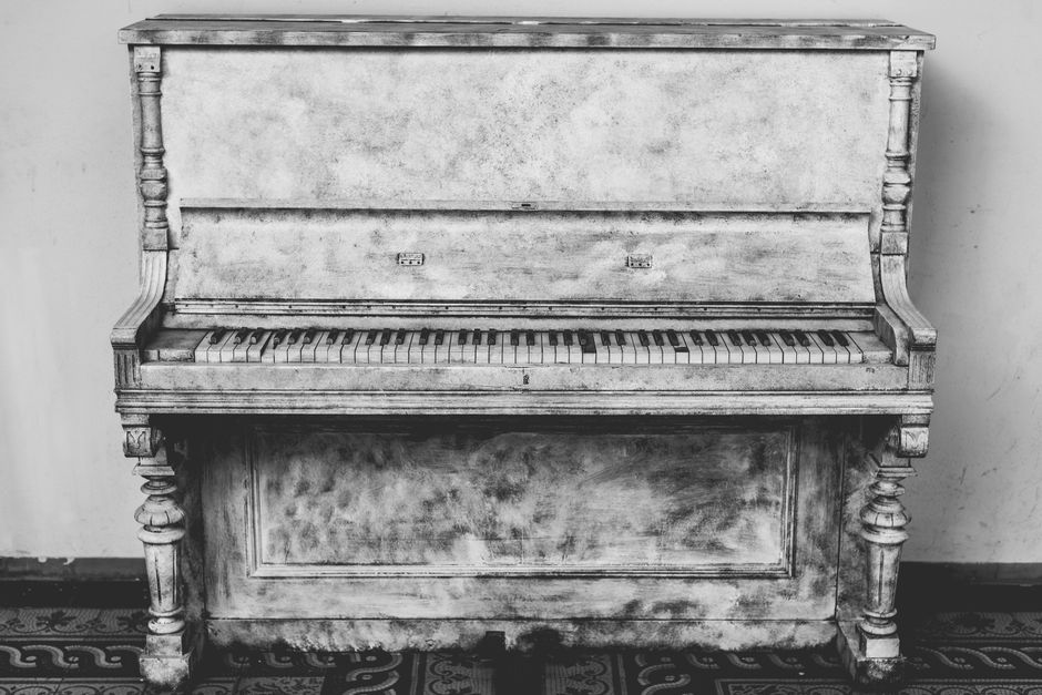Close-up view of the internal mechanisms of a piano, showing the wooden hammers aligned in a row with felt coverings, some dust particles visible on their surfaces. Behind the hammers, metal strings a